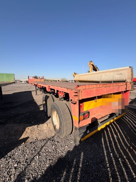 Used 12m flat deck trailer, rear three-quarter view showing the low dropsides and tandem axles