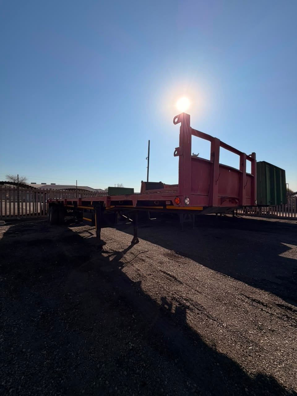 Used 12m flat deck trailer, full length seen from the rear, into low sun