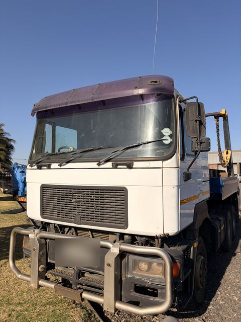Used MAN skip loader truck, front three-quarter view of the white cab and bull bar
