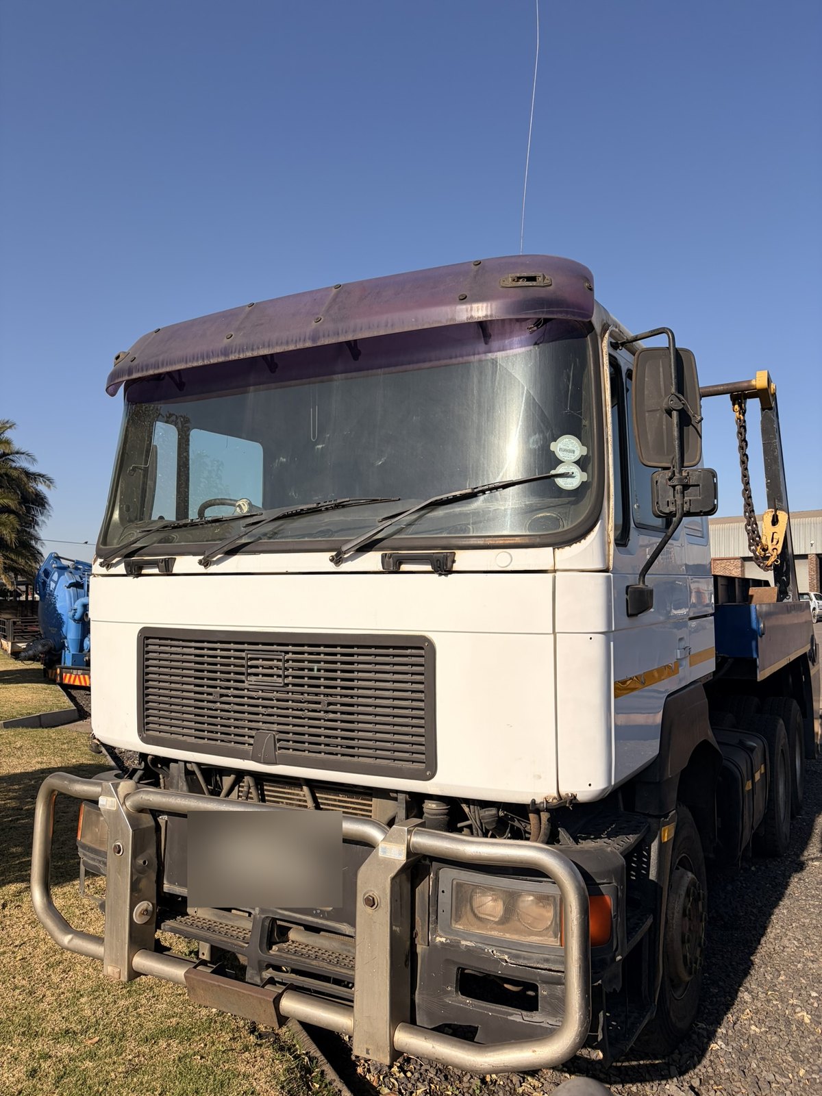 Used MAN skip loader truck, front three-quarter view of the white cab and bull bar