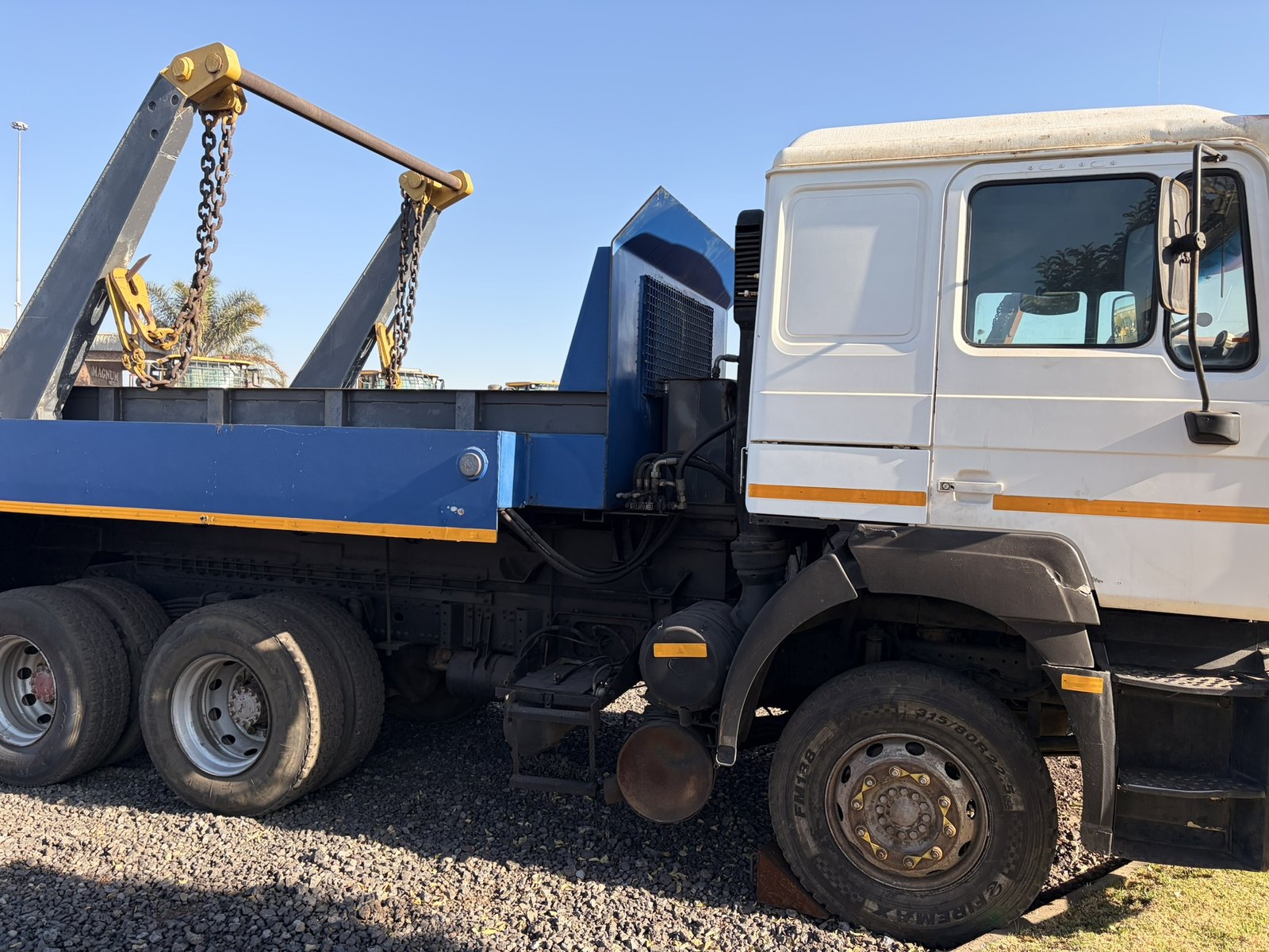 Used MAN skip loader truck, full side profile of the cab and blue skip body