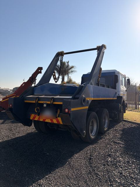 Used MAN skip loader truck, rear three-quarter view of the skip arms and lifting chains