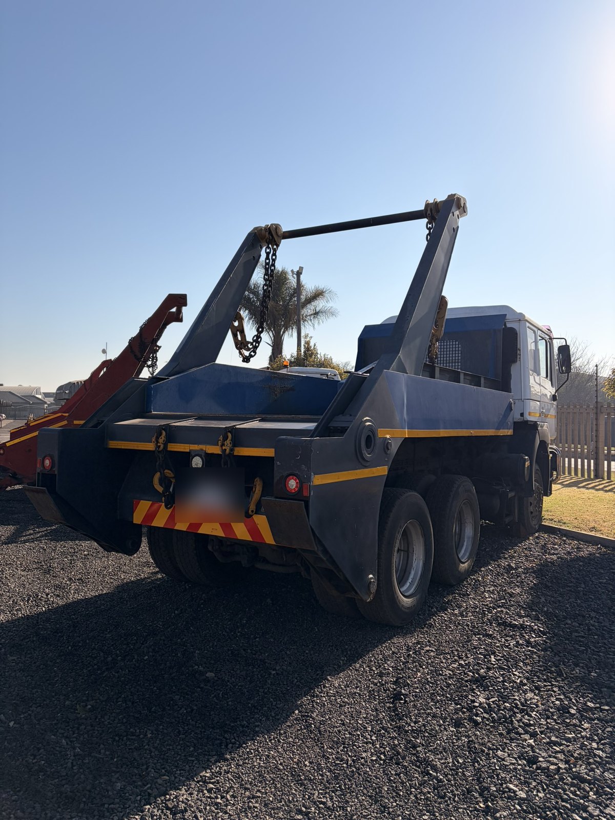 Used MAN skip loader truck, rear three-quarter view of the skip arms and lifting chains