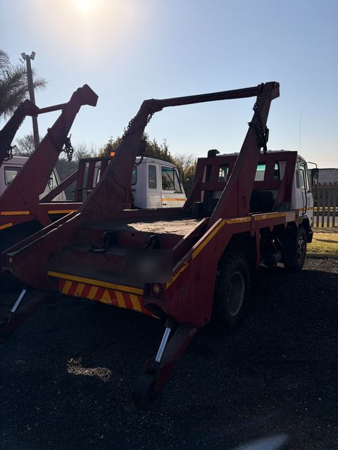 Used Nissan Diesel skip loader truck, rear three-quarter view shot into the sun