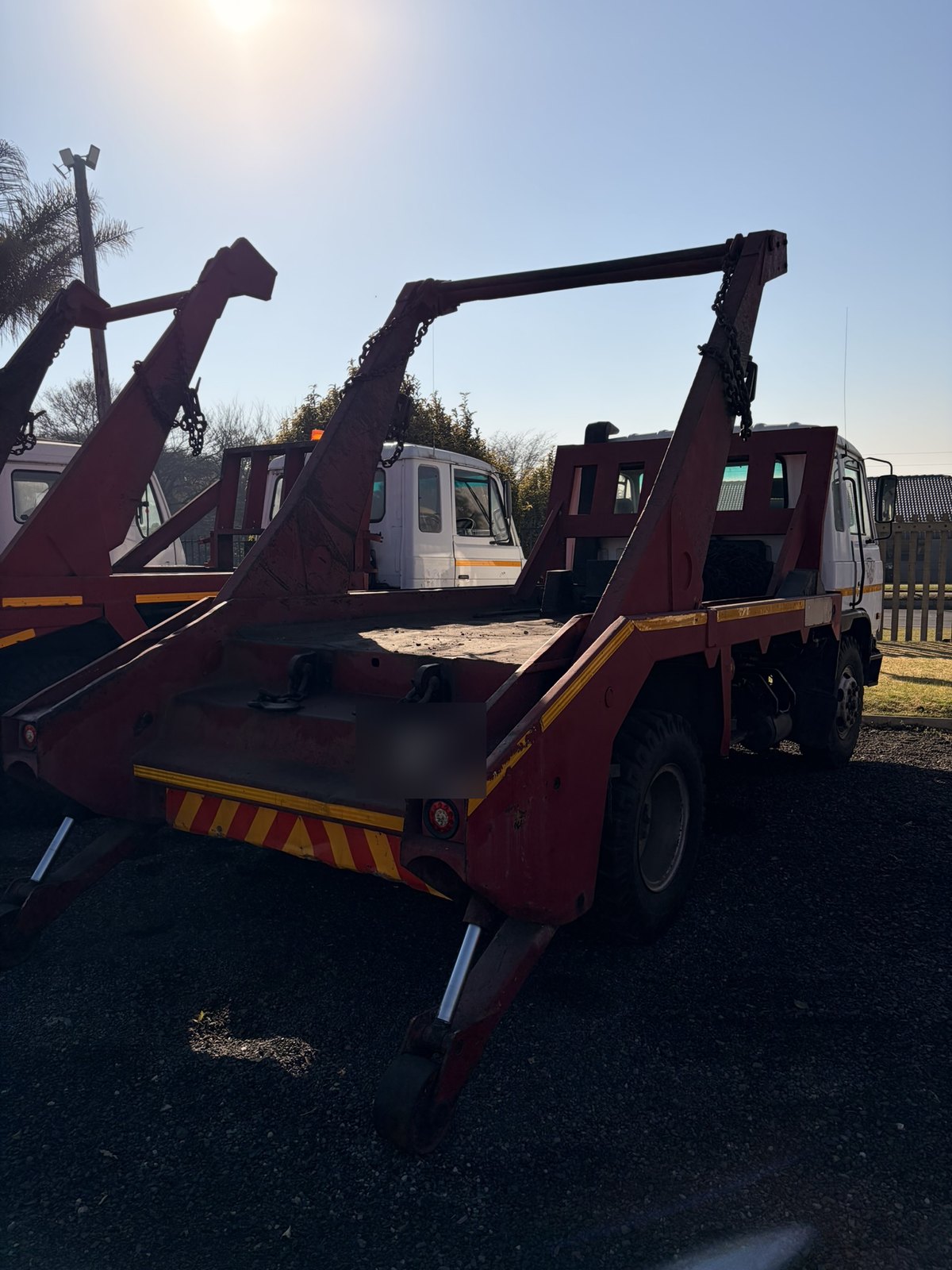 Used Nissan Diesel skip loader truck, rear three-quarter view shot into the sun