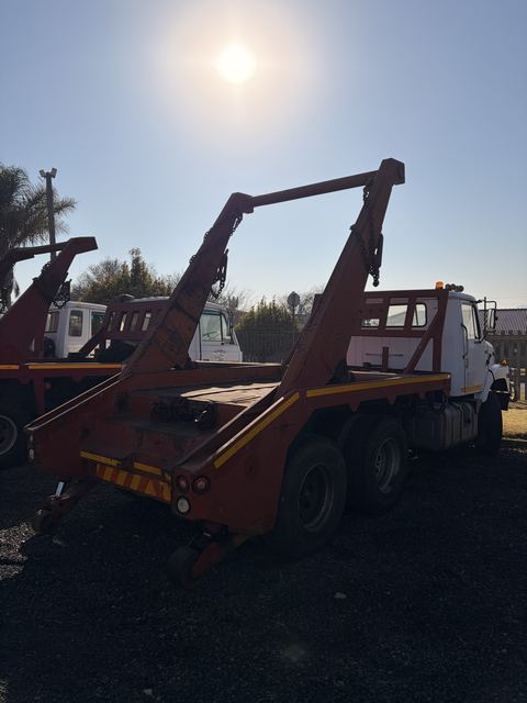 Skip loader truck in the consignment yard, rear three-quarter view of the red skip frame