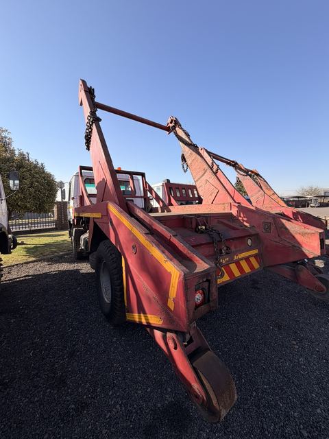Used Nissan Diesel skip loader truck, rear three-quarter view standing among the yard fleet