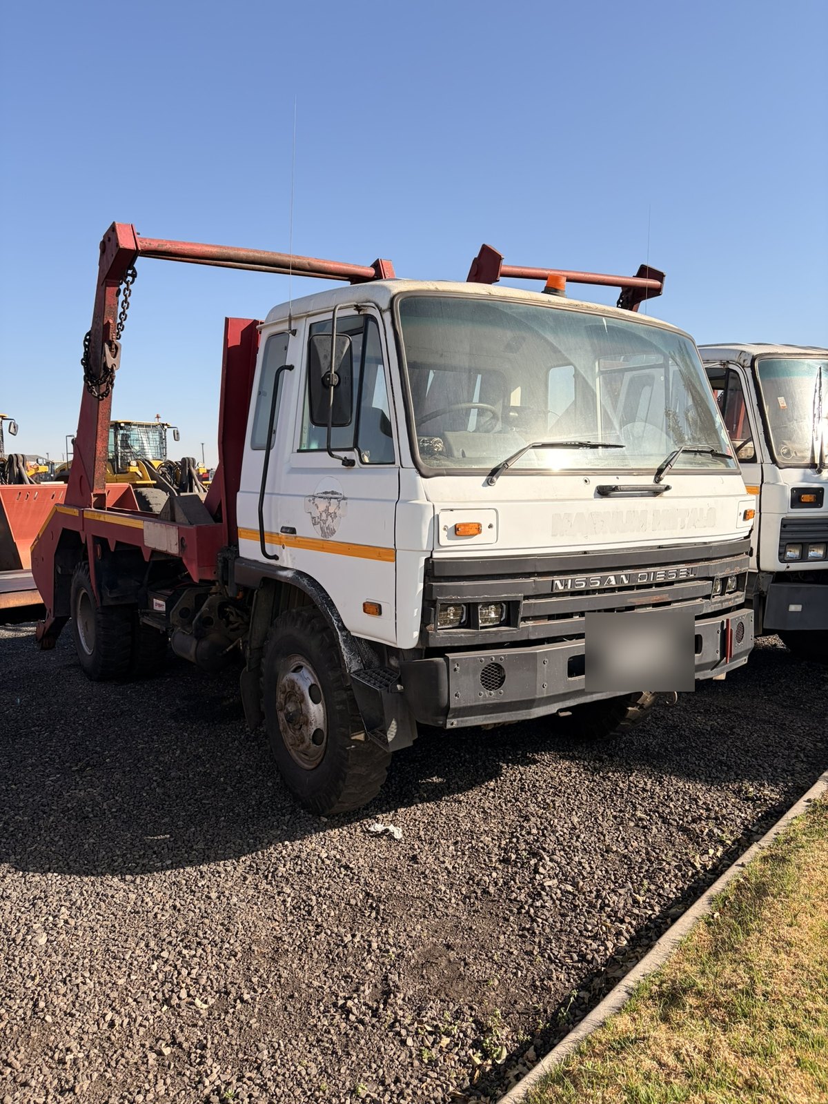 Second used Nissan Diesel skip loader truck, front three-quarter view in the yard