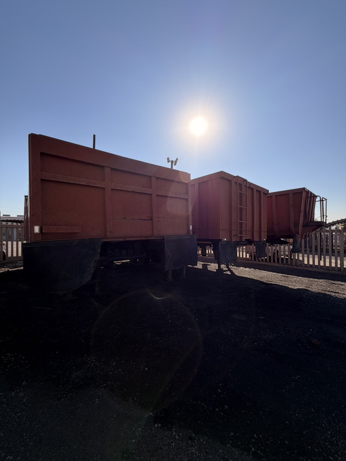 Rear tipper trailers standing coupled in the yard, side view into the late sun