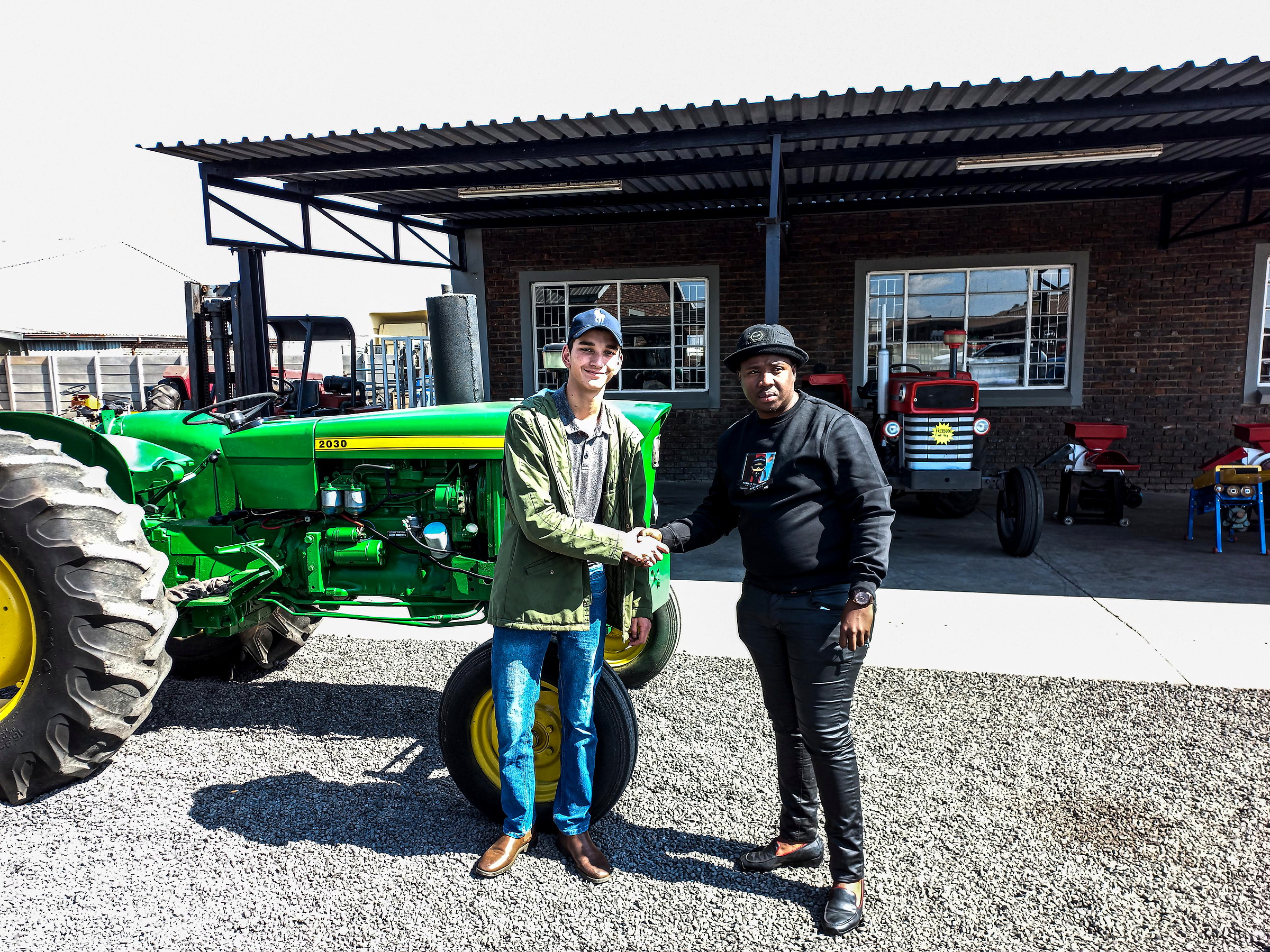 Morne shaking hands with a buyer beside the first tractor he sold